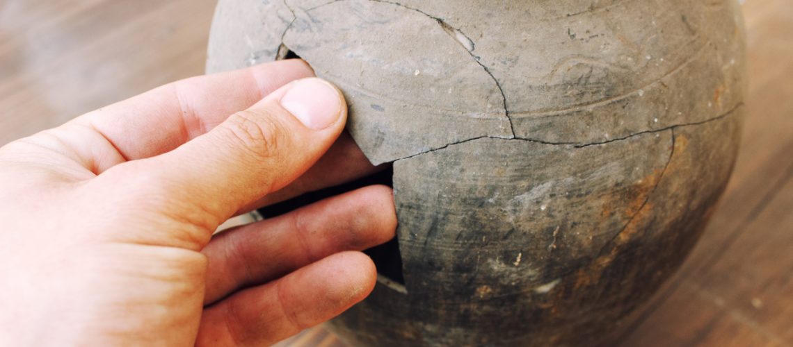 Man hand restoration broken fragments earthenware jug close up view